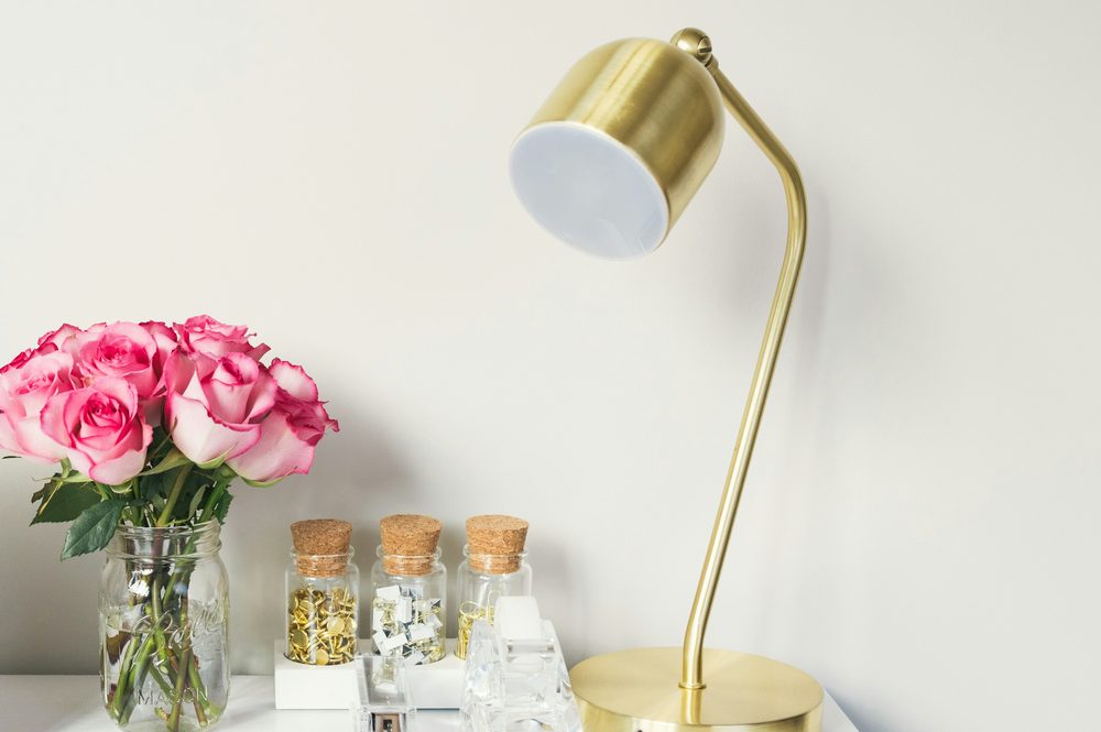 Un bureau clair et rangé, avec une lampe dorée, des roses et des carnets