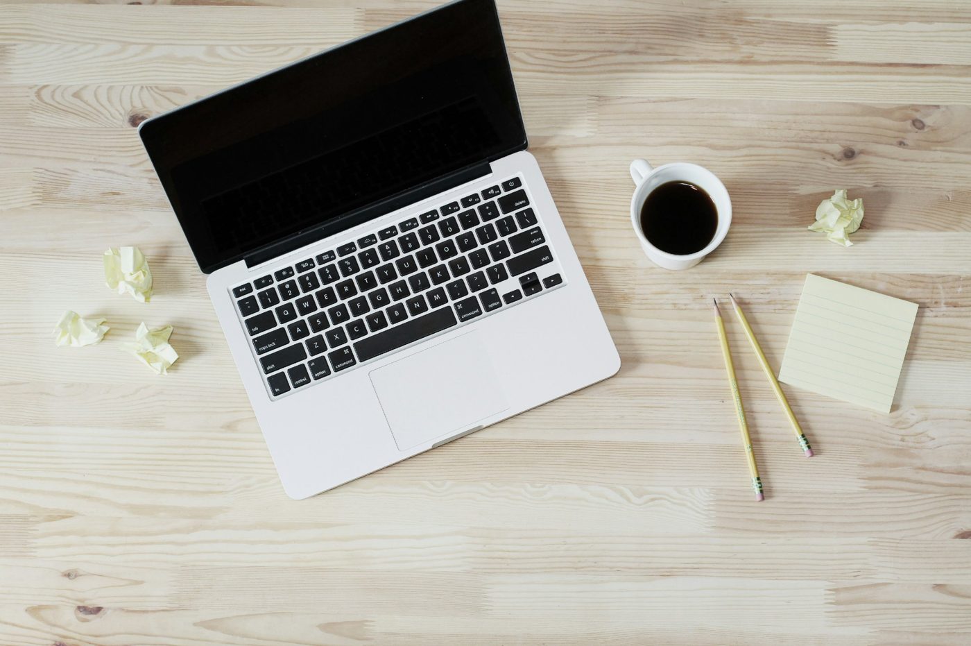 Un ordinateur portable, une tasse de café, des crayons et un bloc-notes sur un bureau en bois clair